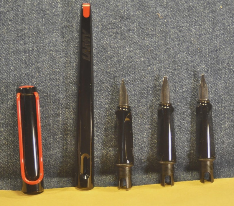K&ouml;nnte beinhalten: Ein schwarzer Lamy-Stift mit roter Akzentfarbe auf der Kappe und einer roten Spitze. Der Stift ist zerlegt und zeigt die Federn und den Stiftk&ouml;rper. Das Lamy-Logo ist auf dem Stiftk&ouml;rper sichtbar.