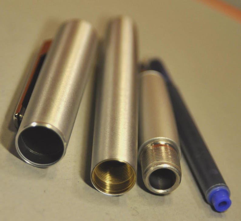 May include: A disassembled silver pen with a blue ink cartridge. The pen's components include the cap with a clip, the main body, and the threaded tip. The interior of the pen's body has a gold-colored finish.