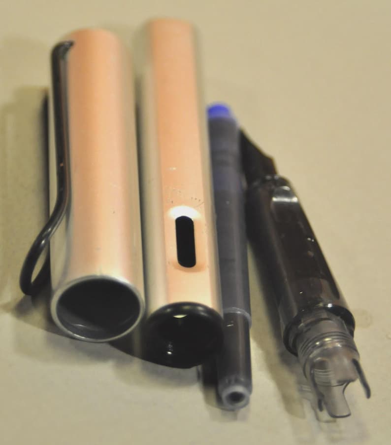 K&ouml;nnte beinhalten: Ein zerlegter F&uuml;llfederhalter bestehend aus einer metallisch silbernen Kappe mit schwarzem Drahtclip, einem passenden silbernen Schaft mit Tintensichtfenster, einer dunkelblauen Tintenpatrone und einem schwarzen Kunststoffgriffst&uuml;ck.
