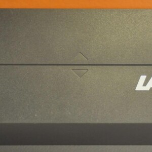 May include: A rectangular, dark gray box with the white word "LAMY" printed on the front. The box has a textured surface and a hinged lid. A small arrow is visible on the top of the box.