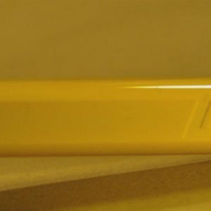 Puede incluir: Primer plano de un barril de bol&iacute;grafo amarillo brillante con el nombre de la marca "LAMY" grabado en relieve en el lateral. El bol&iacute;grafo tiene un acabado liso y brillante y una forma cil&iacute;ndrica. El fondo es amarillo liso y apagado.
