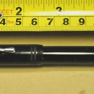 Puede incluir: Una pluma estilogr&aacute;fica negra con un clip de metal plateado colocada debajo de una cinta m&eacute;trica amarilla. La pluma mide aproximadamente 13,3 cm de largo, con un cuerpo cil&iacute;ndrico liso y detalles de anillos horizontales cerca de la tapa.
