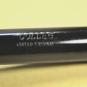 Puede incluir: Una pluma estilogr&aacute;fica negra con acabado brillante que presenta el texto grabado COLLEG y KAWECO-FABRIKAT en el cuerpo. El cuerpo de la pluma tiene una forma cil&iacute;ndrica con detalles de anillos horizontales cerca de la tapa.