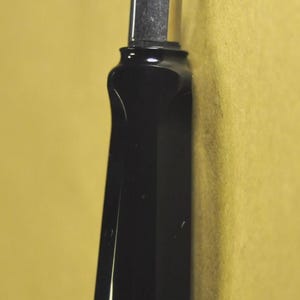 K&ouml;nnte beinhalten: Nahaufnahme eines schwarzen F&uuml;llfederhalters mit silberner Feder. Der Stift hat ein schlankes, modernes Design mit gl&auml;nzendem Finish. Die Feder ist spitz und scheint zum Schreiben bereit zu sein. Der Hintergrund ist einfarbig, ged&auml;mpftes Gelb.