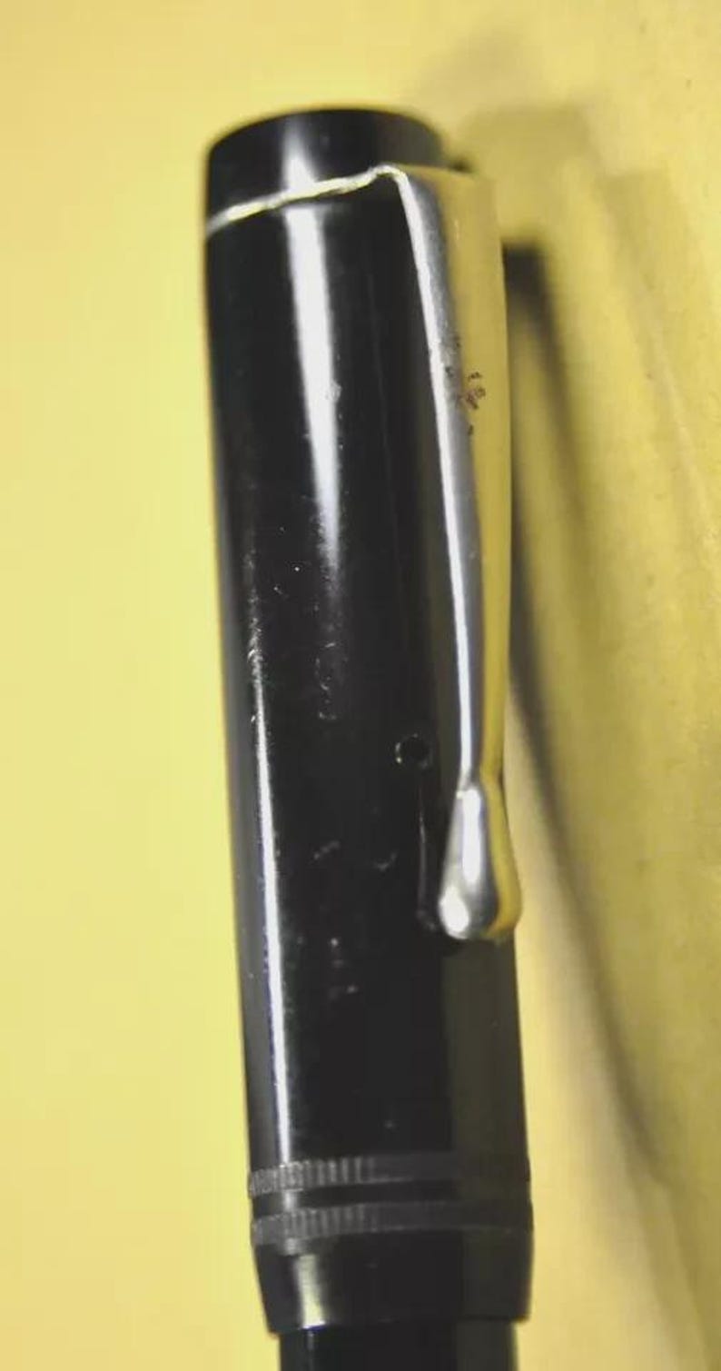 Puede incluir: Un capuch&oacute;n de pluma estilogr&aacute;fica negro con un clip de metal plateado pulido fijado en la parte superior. El capuch&oacute;n tiene un acabado liso y brillante con dos finas l&iacute;neas horizontales grabadas que rodean la secci&oacute;n inferior cerca de la base.
