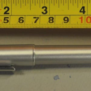 Może przedstawiać: Srebrny długopis z klipsem obok ż&oacute;łtej miarki. Długopis ma około 14 cm długości. Miarka pokazuje pomiary w stopach i calach.