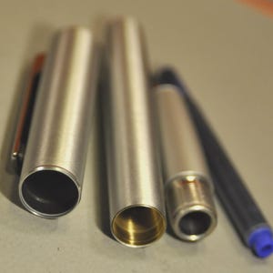 May include: A disassembled silver pen with a gold-colored interior. The pen's components include the cap, barrel, and ink cartridge. The blue ink cartridge has a blue tip.