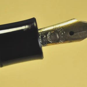 Puede incluir: Una pluma estilogr&aacute;fica negra con un plum&iacute;n de metal dorado. El plum&iacute;n presenta un logotipo circular grabado y el texto 4C58. La pluma tiene una secci&oacute;n de agarre negra lisa y un cuerpo acanalado, mostrando un dise&ntilde;o cl&aacute;sico de escritura.
