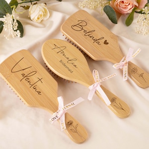 Peut inclure: Brosses à cheveux en bois personnalisées avec les noms de Valentina, Amelia (Demoiselle d'honneur) et Belinda. Chaque brosse est ornée d'un motif floral et d'un ruban rose. Sur une surface blanche avec des fleurs.