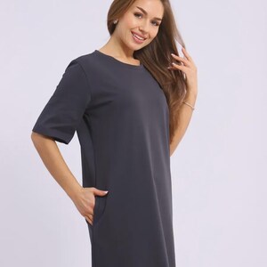 May include: A dark grey, short-sleeved dress with a round neckline and pockets. The dress is a solid colour and appears to be made of a soft, flowing fabric. The dress is knee-length.