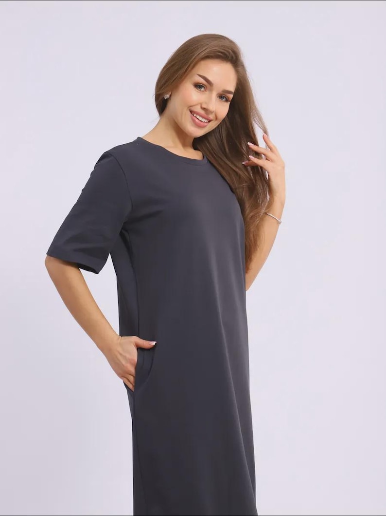May include: A dark grey, short-sleeved dress with a round neckline and pockets. The dress is a solid colour and appears to be made of a soft, flowing fabric. The dress is knee-length.
