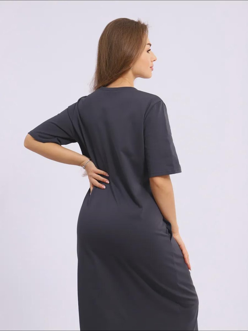 May include: A charcoal grey t-shirt dress with short sleeves and a knee-length hem. The dress has a simple, minimalist design, suitable for casual wear. The model is wearing a silver bracelet.