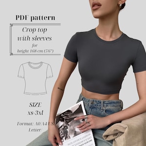 Puede incluir: Un top corto gris oscuro con mangas cortas. La imagen incluye un patrón PDF para el top, con texto que indica tallas de XS a 3XL y una altura de 168 cm. El patrón es para un top corto con mangas.