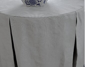 May include: A white table cloth with a blue and white patterned bowl filled with white roses. The table cloth has a black trim around the bottom.