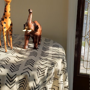 May include: A round table with a white tablecloth featuring a black chevron pattern. A wooden giraffe and elephant figurine are on the table.