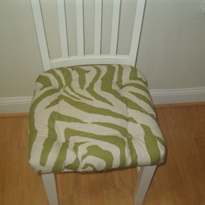 May include: A white chair with a green and white zebra print cushion.