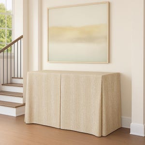 May include: A beige cabinet with a textured, reptile-like pattern. The cabinet has two doors and is positioned beneath a framed abstract painting with soft, muted colors. The room features a staircase and hardwood flooring.