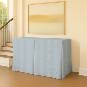 May include: A light blue cabinet with a textured pattern, set against a neutral wall and wooden floor. The cabinet is rectangular with a curved front. A framed abstract painting hangs above the cabinet.