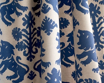 May include: Close-up of a fabric with a repeating pattern of blue lions and floral motifs on a cream background. The fabric is draped, showing folds and texture. The design has a classic, regal feel.