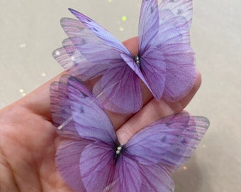 May include: Two purple butterfly embellishments with a sparkly center. The butterflies are made of sheer fabric and have a delicate, feminine look.