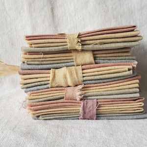 Peut inclure: Plusieurs piles de tissus pliés aux couleurs douces, rose, jaune et gris, sont liées avec de la ficelle naturelle. Le tissu, probablement du lin ou une matière similaire, donne un aspect rustique. Les paquets sont bien rangés.