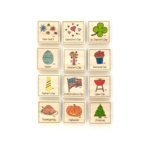 May include: A set of 12 wooden stamps featuring holiday and seasonal themes. Each stamp has a different image and text, such as "New Year's", "Valentine's Day", "St. Patrick's Day", "Easter", "Mother's Day", "Memorial Day", "Father's Day", "Independence Day", "Labor Day", "Thanksgiving", "Halloween", and "Christmas".