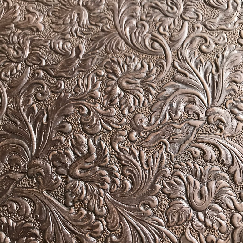 May include: A close-up of a brown embossed fabric with a floral pattern. The fabric has a textured surface and a rich, dark brown color.
