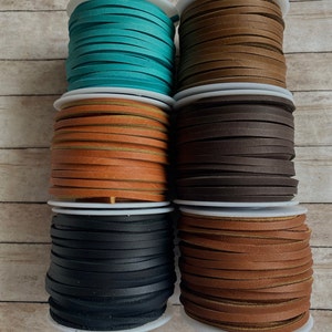 May include: Six spools of leather cord in various colors, including teal, brown, black, and tan. The spools are stacked on a wooden surface.