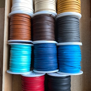 May include: Assortment of 10 spools of leather cord in various colors, including white, beige, brown, gray, blue, turquoise, red, and black. The spools are arranged in two rows of five, with the spools in each row alternating in color.