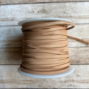 May include: A spool of light brown leather cord. The cord is wound tightly around a white plastic spool.