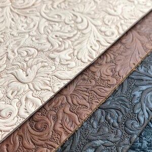 May include: Close-up of three pieces of embossed leather in different colors: white, brown, and black. The leather has a floral pattern.