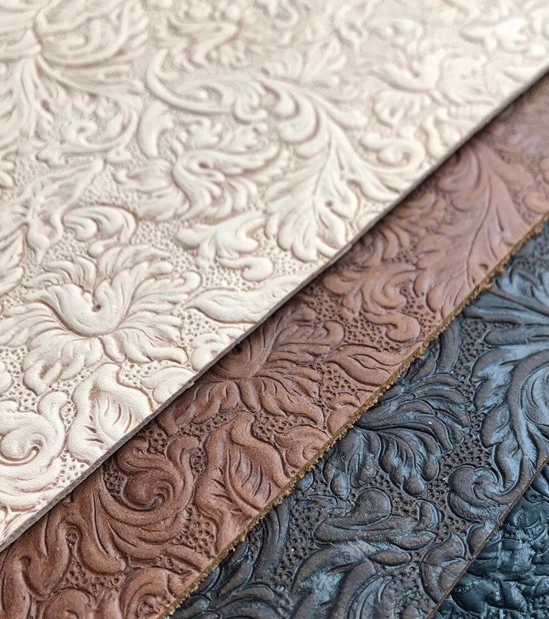 May include: Close-up of three pieces of embossed leather in different colors: white, brown, and black. The leather has a floral pattern.