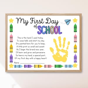 Może przedstawiać: Oprawiony wydruk z napisem "My First Day of School" w czarnych i kolorowych literach. Wydruk zawiera żółty odcisk dłoni, wiersz i ilustracje kredek. Przewidziano miejsce na imię dziecka.