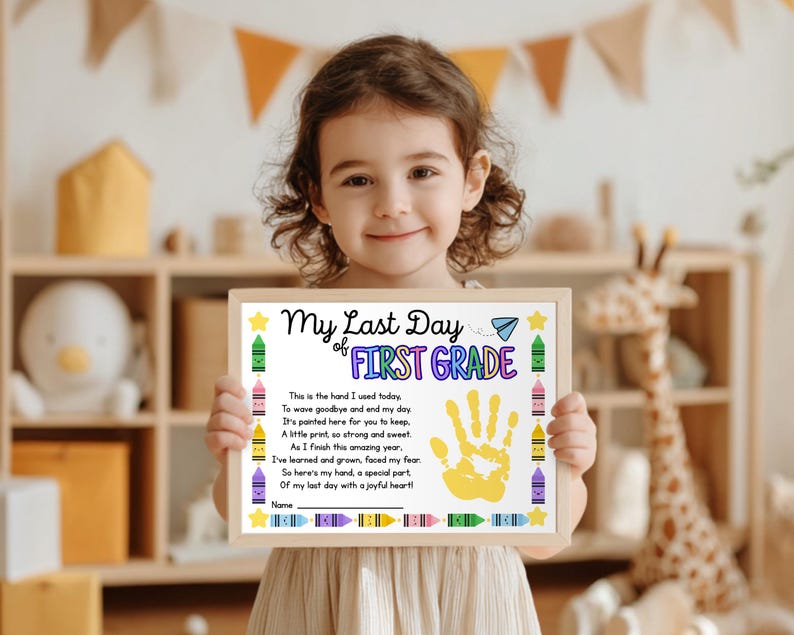 May include: A young child is holding a framed certificate. The certificate says "My Last Day of First Grade" and features a yellow handprint and crayon illustrations. The background includes a wooden shelf and toys.