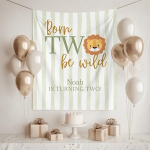 May include: A rectangular fabric backdrop featuring vertical sage green and white stripes with the text Born TWO be wild and a cartoon lion face. Below, the text reads Noah IS TURNING TWO! The backdrop is surrounded by metallic gold and white balloons.