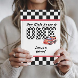 Peut inclure: Un livre blanc avec une bordure à carreaux rouges et noirs et le texte "Our little Racer is ONE". Le mot "ONE" est dans un motif à carreaux. Une voiture de course de dessin animé est également présentée. Le texte "Letters to Edward" est en dessous.