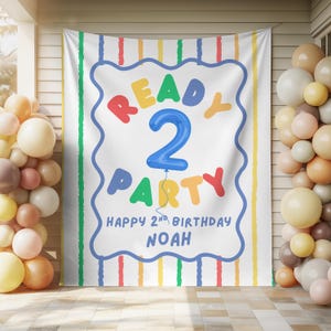 Puede incluir: Un telón de fondo rectangular blanco para fiestas con rayas verticales de colores y un marco central azul de bordes ondulados. El texto dice READY 2 PARTY, HAPPY 2ND BIRTHDAY y NOAH, con un gran número 2 azul en forma de globo.