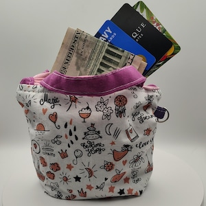 May include: A small, white fabric pouch with a pink rim and a whimsical pattern of hearts, stars, and dream catchers. The pouch contains cash and several credit cards. The word "Magic" is visible on the pouch.