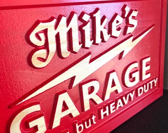 May include: Red wooden sign with the words "Mike's Garage" in a vintage font, with a lightning bolt design. The sign also includes the phrase "Nothing but Heavy Duty" in white lettering. The sign is a decorative item.