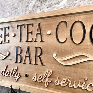 K&ouml;nnte beinhalten: Ein Holzschild mit dem Text "Coffee - Tea - Cocoa - Bar" und den Worten "open daily - self service" in einer kursivschrift.