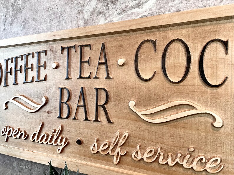 K&ouml;nnte beinhalten: Ein Holzschild mit dem Text "Coffee - Tea - Cocoa - Bar" und den Worten "open daily - self service" in einer kursivschrift.
