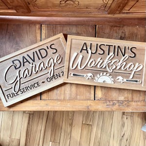 May include: Two wooden signs with carved lettering. The first sign says "David's Garage - Full Service - Open?" The second sign says "Austin's Workshop" with a saw blade and wrench design.