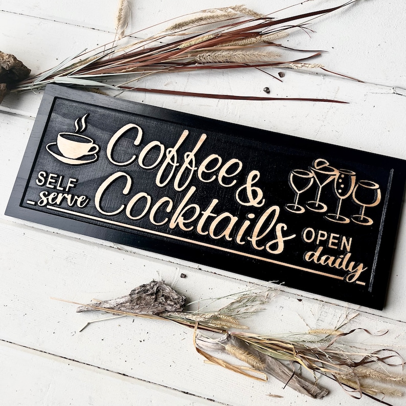 May include: Black wooden sign with gold lettering that reads "Coffee & Cocktails" and "Open Daily". The sign also features a coffee cup and four cocktail glasses.