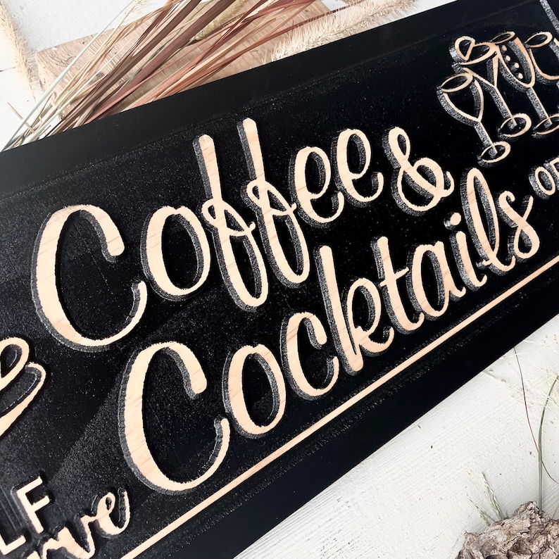 May include: Black wooden sign with the text "Coffee & Cocktails" in a light wood font. The sign has a decorative border and a small image of three glasses with a bow on top.