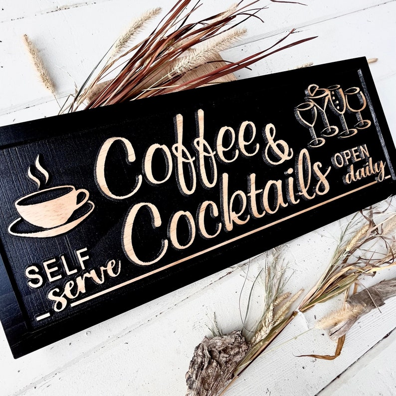 May include: Black wooden sign with white lettering that reads "Coffee & Cocktails" and "Self Serve". The sign also has a gold silhouette of a coffee cup and a few cocktail glasses. The sign also says "Open Daily" in gold lettering.