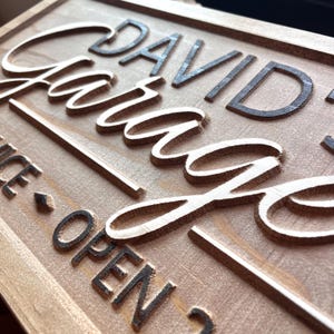 May include: A wooden sign with the text "David's Garage" in black lettering. The sign also has the text "Nice - Open" in black lettering.