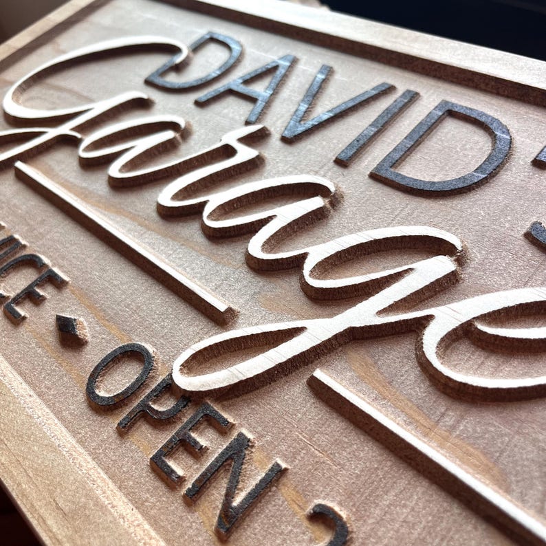 May include: A wooden sign with the text "David's Garage" in black lettering. The sign also has the text "Nice - Open" in black lettering.