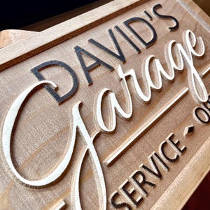 May include: A wooden sign with the text "DAVID'S Garage" in black lettering and "SERVICE" in black lettering below. The word "Garage" is in white raised lettering.