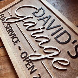 May include: A wooden sign with the text "David's Garage" in black lettering. The sign also says "Full Service - Open 24/7".