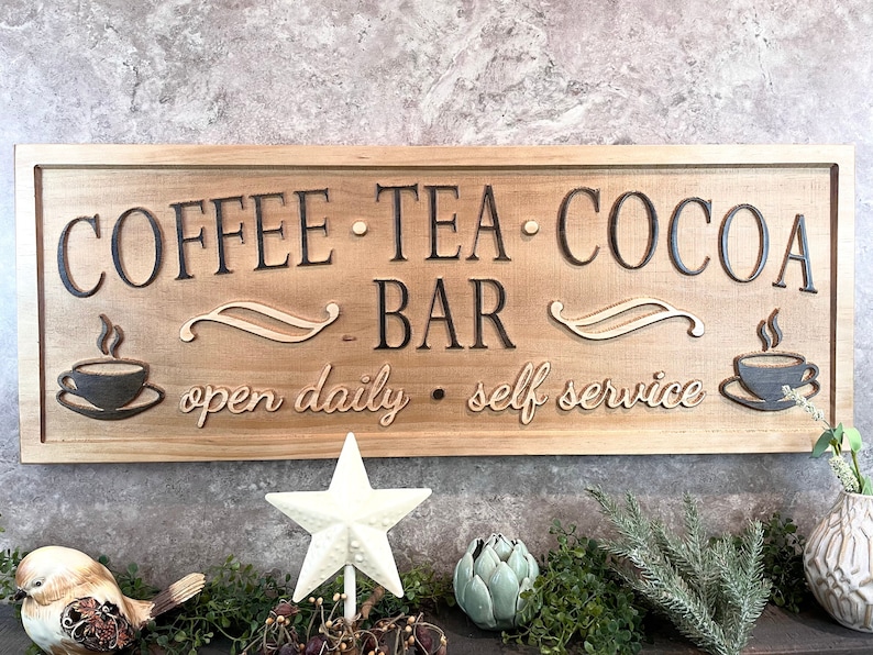 K&ouml;nnte beinhalten: Ein Holzschild mit dem Text "COFFEE - TEA - COCOA - BAR" und den Worten "open daily - self service" in einer kursivschriftlichen Schriftart. Das Schild hat zwei stilisierte Kaffeetassen mit Dampf, der aus ihnen aufsteigt.